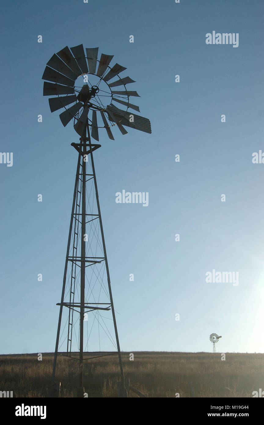 windmills silhouetted against blue sky in barren paddock, Queensland, Australia. Windmills are commonly used for pumping water from bores or dams to t Stock Photo