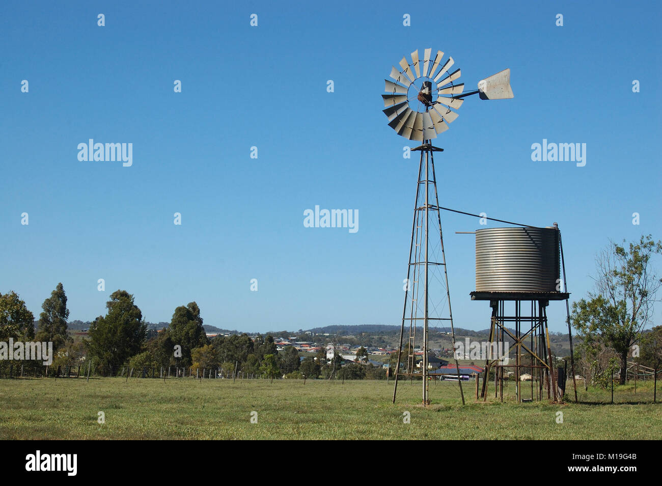Windmill and tankstand in paddock, Queensland, Australia. Windmills are commonly used for pumping water from bores or dams to troughs for livestock. Stock Photo