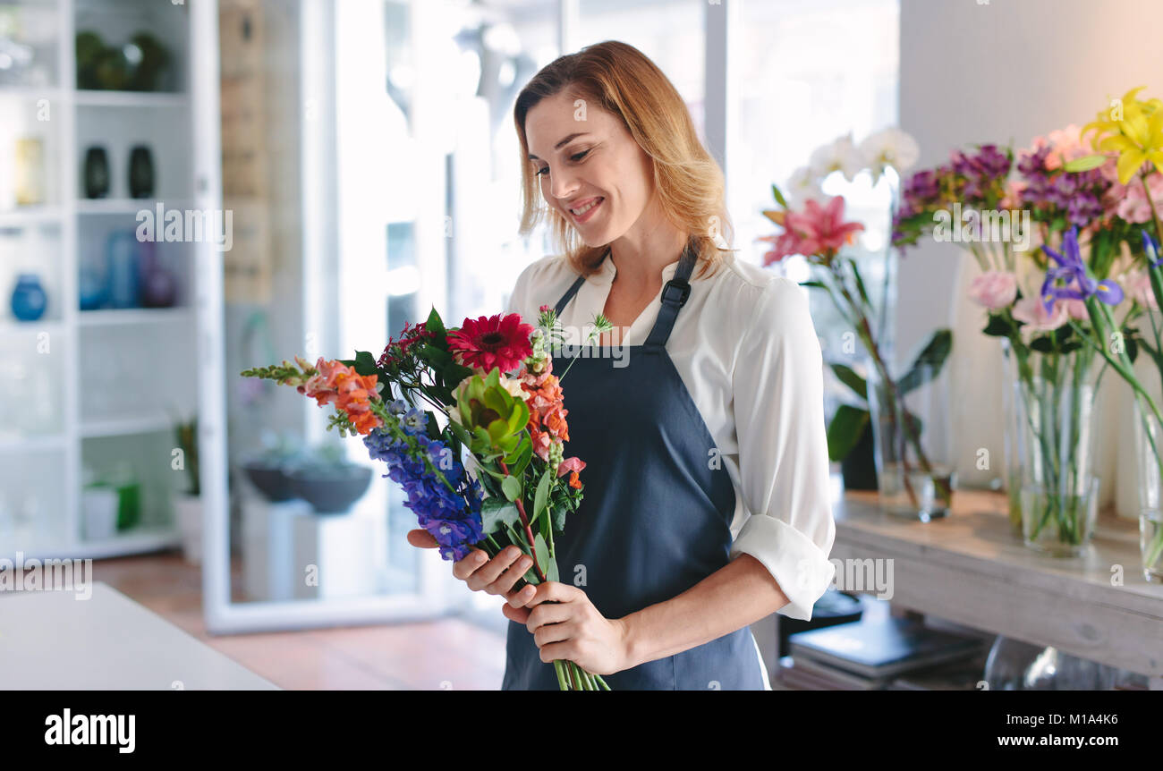 Happy female florist creating bouquet of flowers at her shop. Woman florist with a bouquet at workshop. Stock Photo