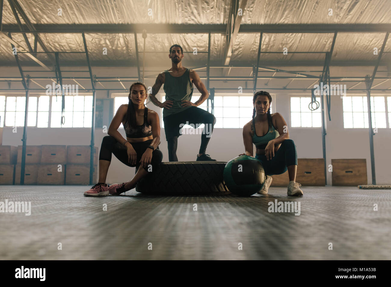 Portrait of three young people resting and looking at camera after training session in gym. Small group of people after training at health club. Stock Photo