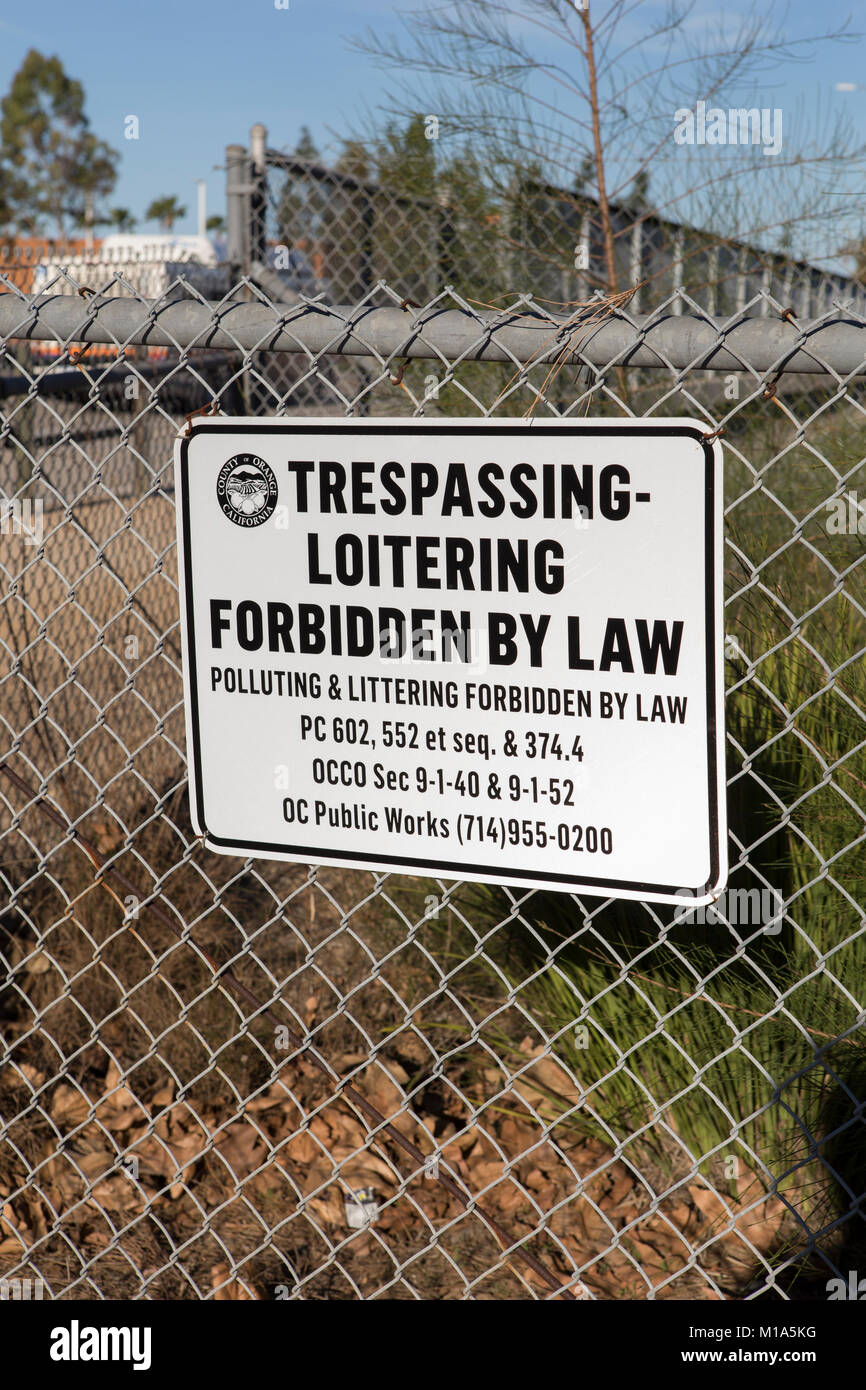 Trespassing and loitering forbidden by law sign posted on a metal fence in an urban setting in Irvine California USA Stock Photo