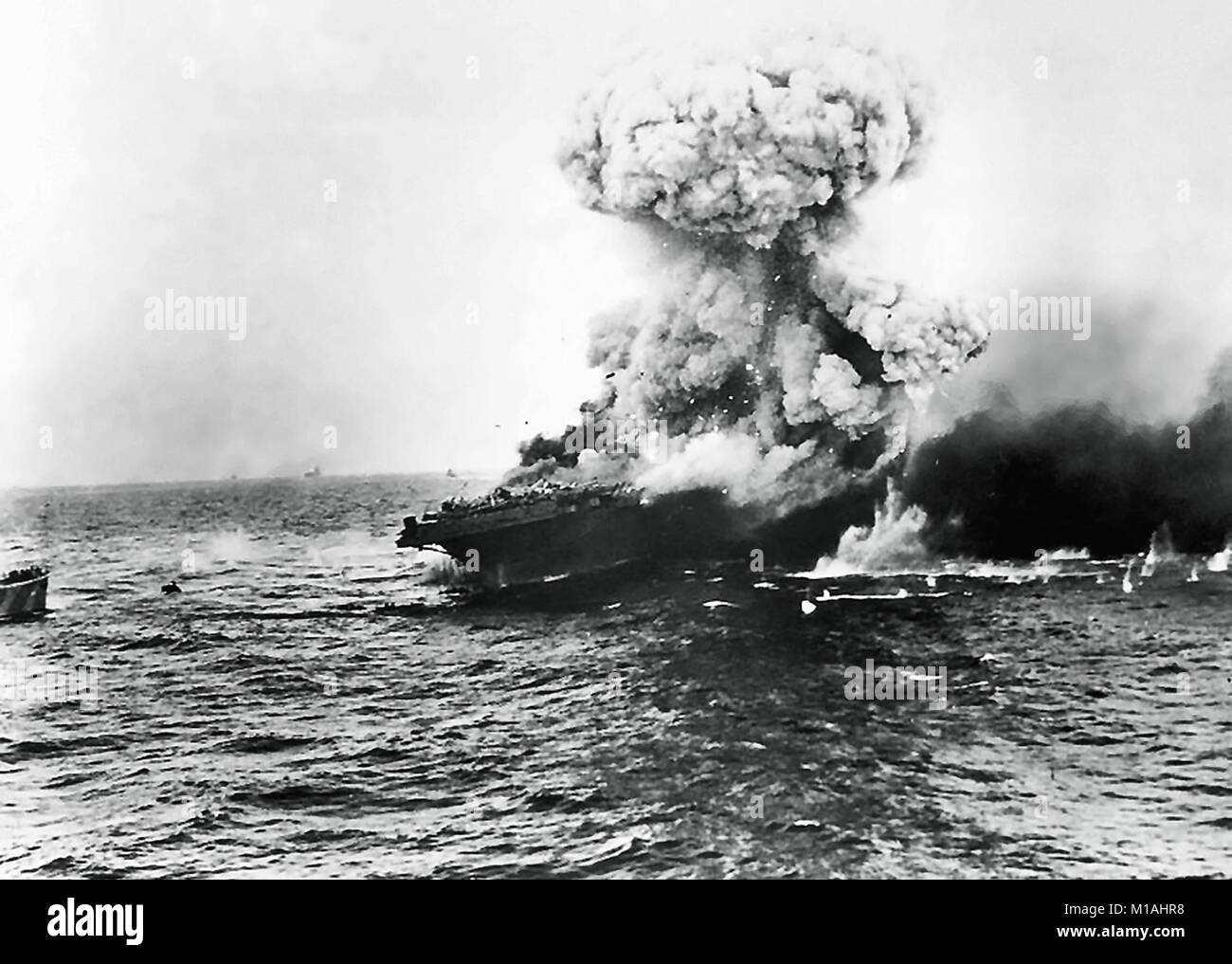 Battle of the Coral Sea, May 1942. A 'mushroom cloud' rises after a heavy explosion on board USS Lexington (CV-2), 8 May 1942. This is probably the 'great explosion' from the detonation of torpedo warheads stowed in the starboard side of the hangar, aft, that followed an explosion amidships at 1727 hrs. Note USS Yorktown (CV-5) on the horizon in the left center, and destroyer USS Hammann (DD-412) at the extreme left. Stock Photo
