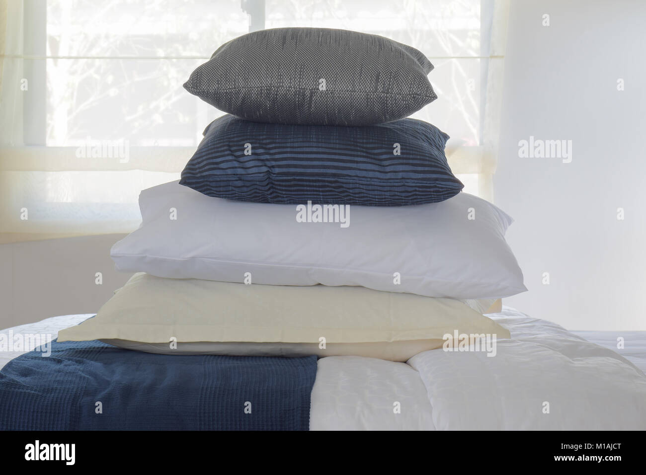 Stacking pillows on bed with wall and window in background Stock Photo