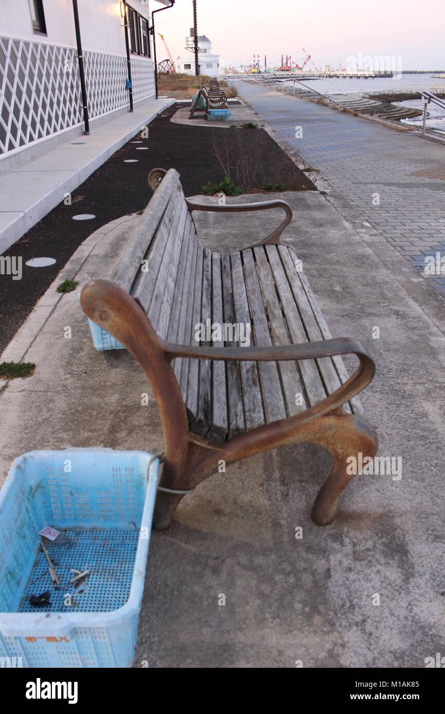 4 November 2015 , Soma, Fukushima, Japan, wood chair with rusty arm rest at the side walk  by Matsuakwaura Beach, Soma, Japan. These benches were swallowed by Tsunami in 2011 but were not destroyed. The blue basket is used as trash bin. Stock Photo
