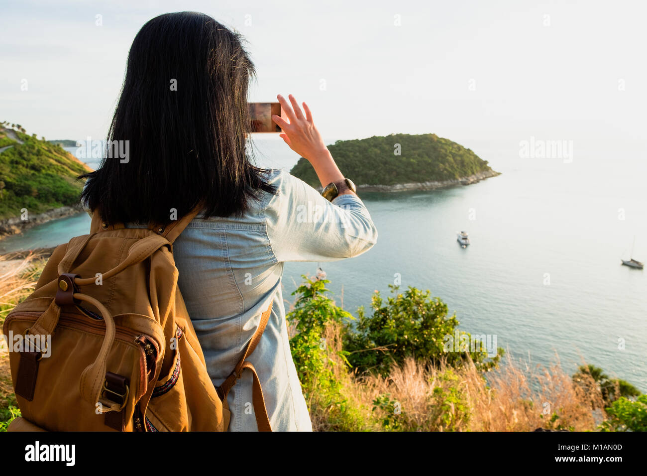 Asia Young traveler woman backpacker use mobile phone take a photo of beautiful of sunset nature at top of mountain sea view,Freedom wanderlust concep Stock Photo