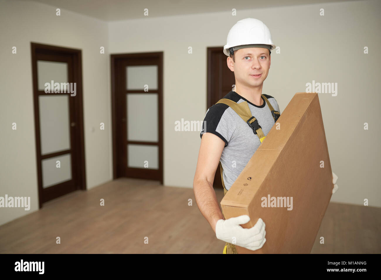 Delivery man with box indoors. Furniture delivery background. Stock Photo