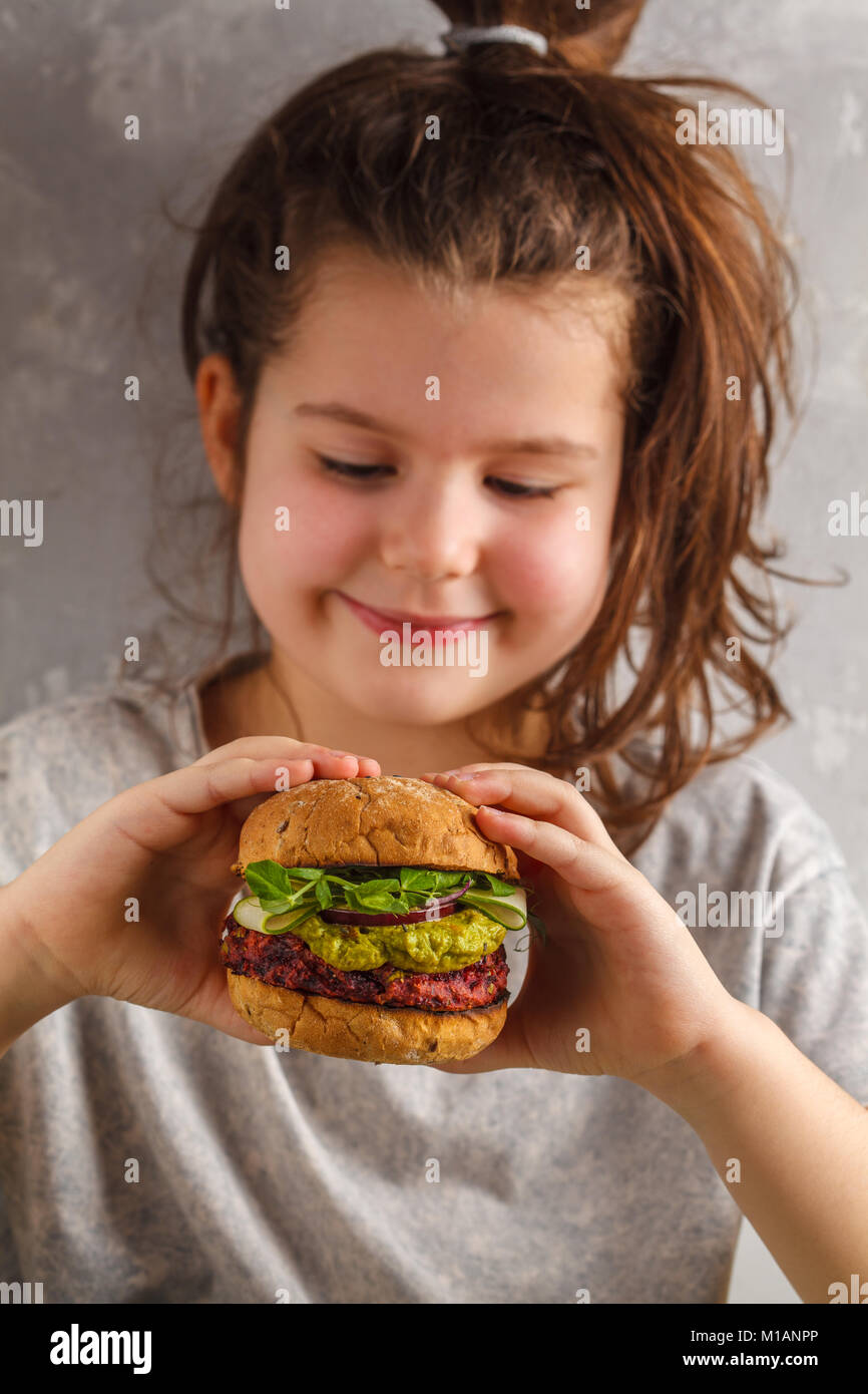 Beautiful happy hungry baby girl eating vegan burger. Vegan beet