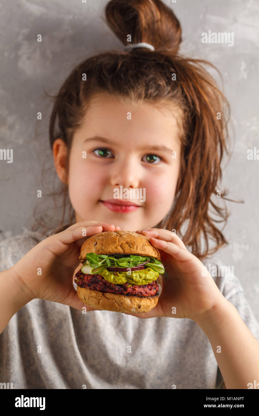 Beautiful happy hungry baby girl eating vegan burger. Vegan beet