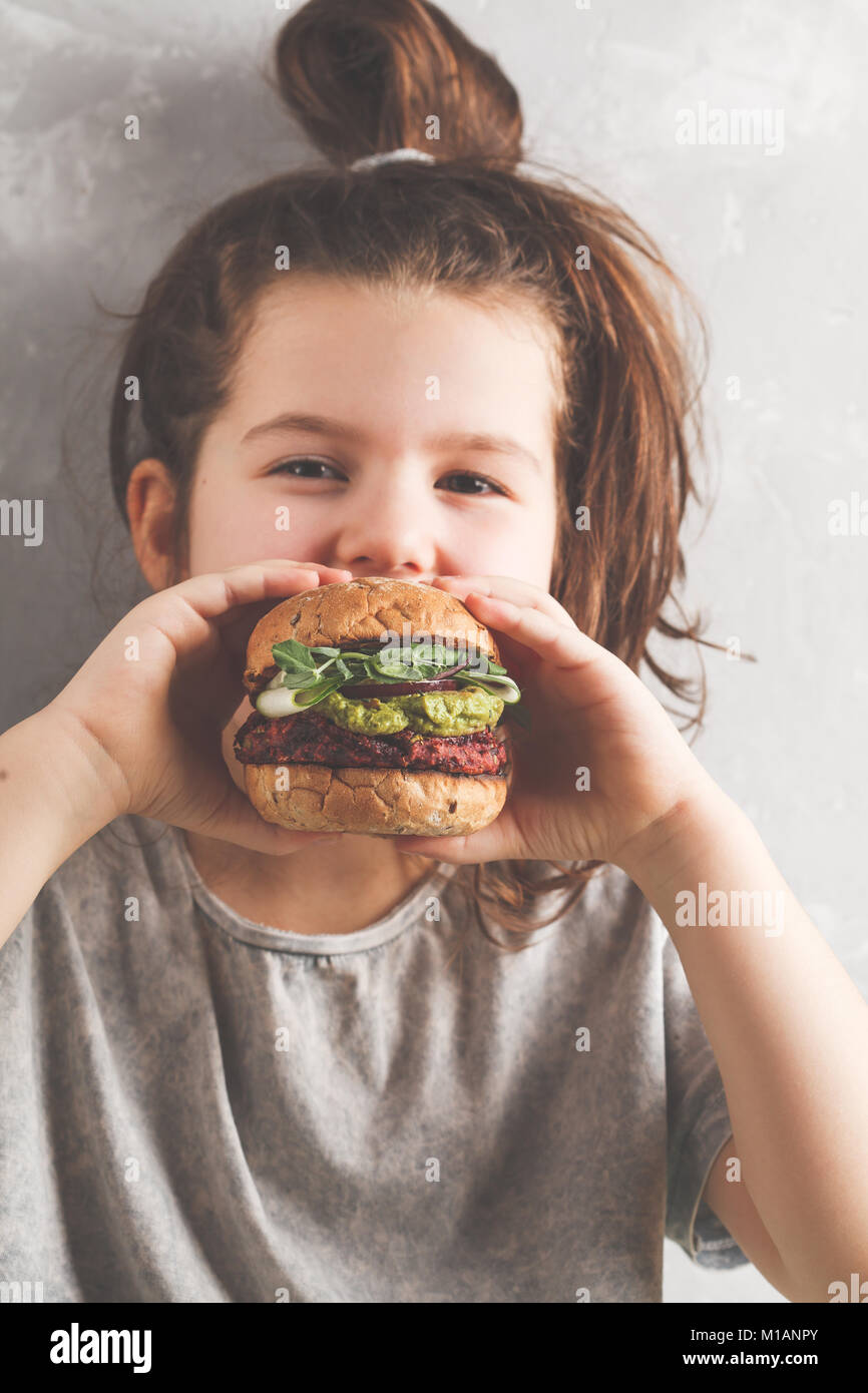 Beautiful happy hungry baby girl eating vegan burger. Vegan beet