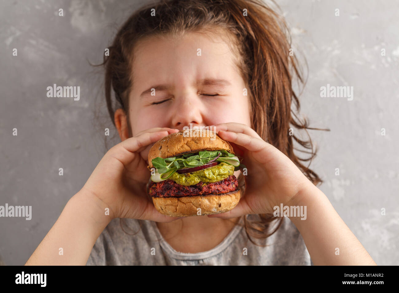 Beautiful happy hungry baby girl eating vegan burger. Vegan beet