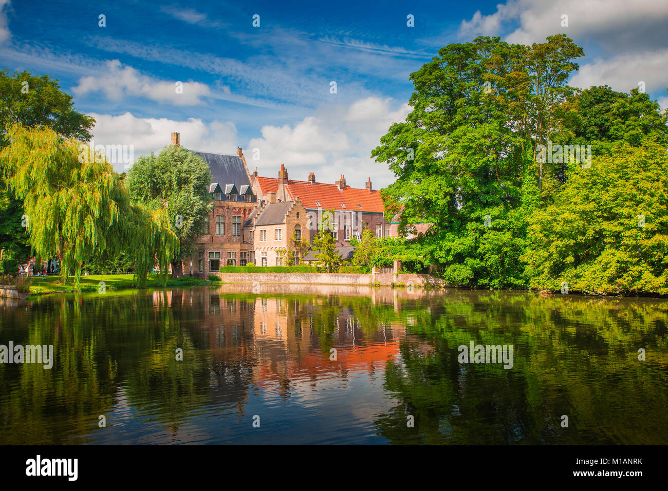 Brugge sunny cityscape. Old buildings of Bruges and green trees reflected in lake. Historical center of Europe. Stock Photo