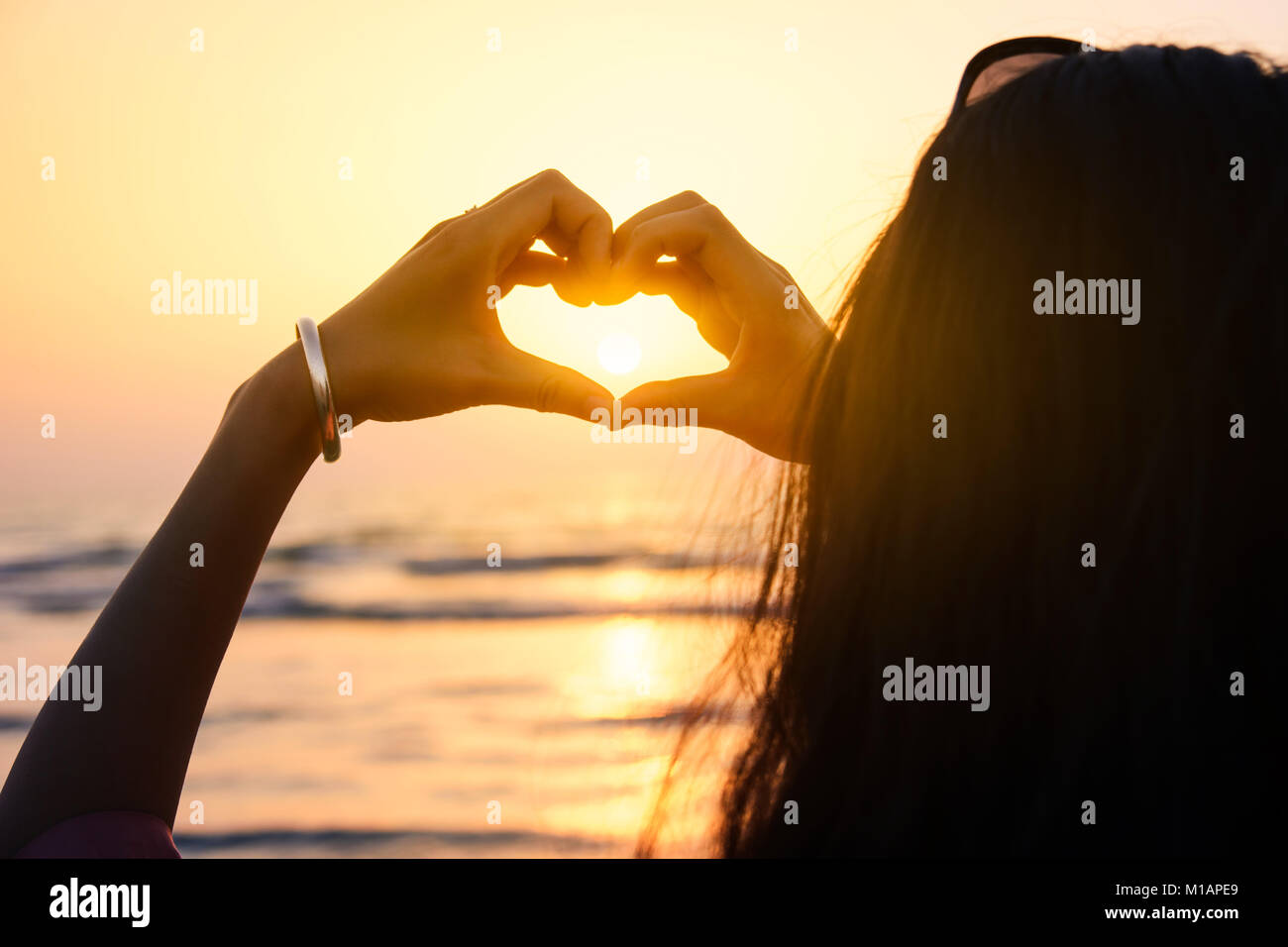 Girl making heart shape with hands in the sunset by seaside Stock Photo