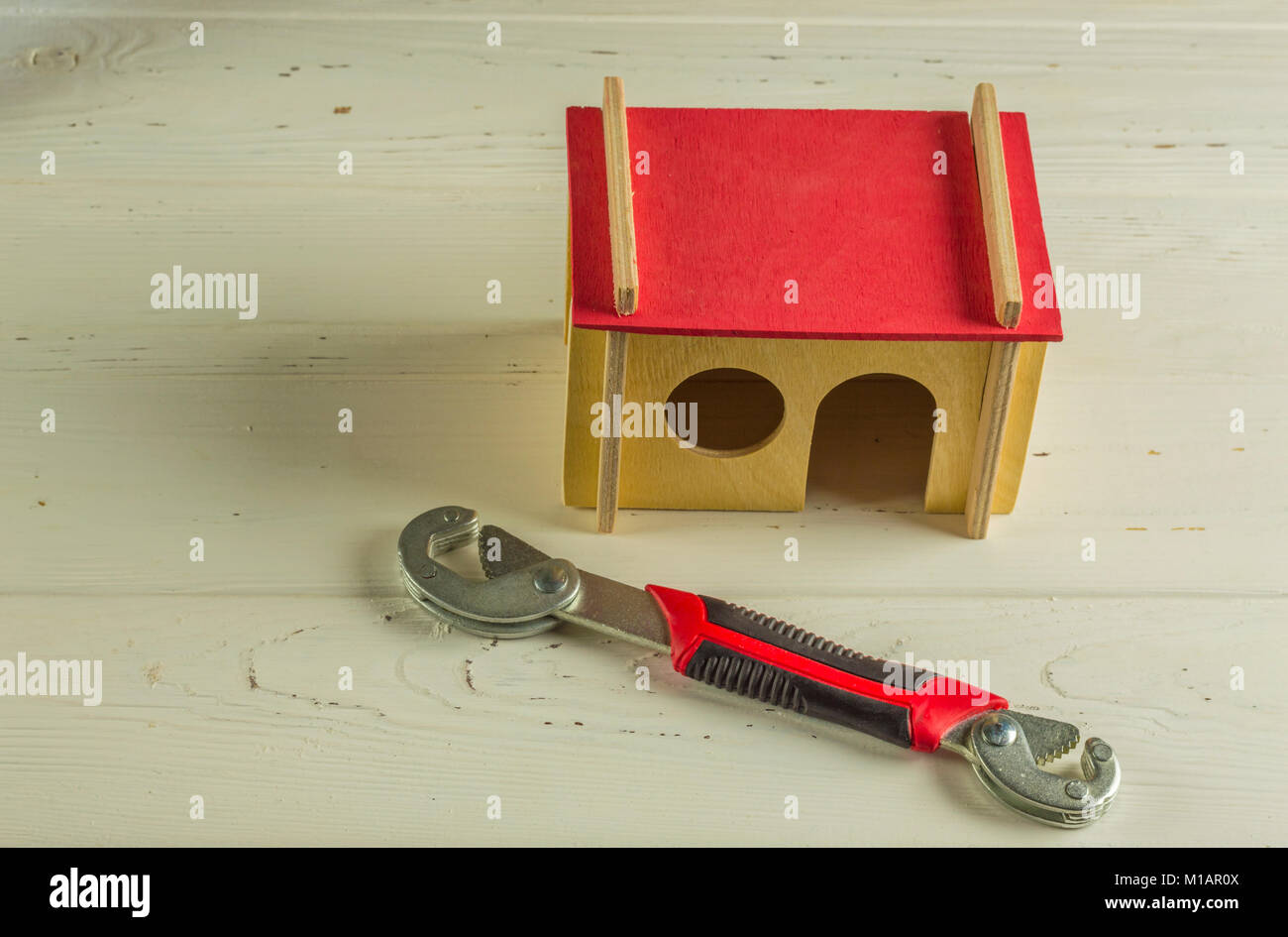 Monkey wrench and model house on wooden background Stock Photo