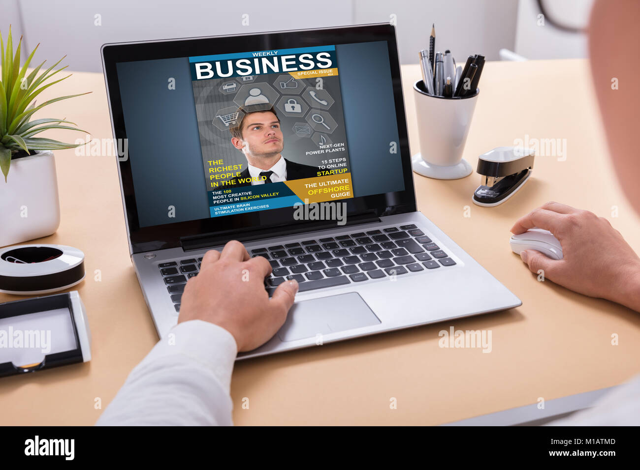 Businessperson Looking At Business Magazine On Laptop At Office Desk Stock Photo
