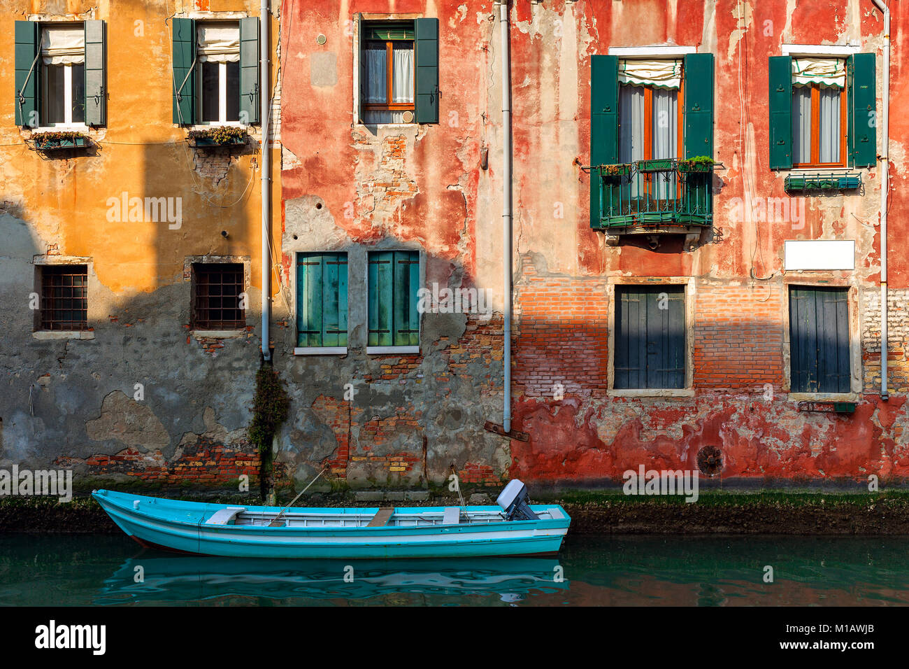 Boat on small canal moored against old colorful brick house in Venice, Italy. Stock Photo