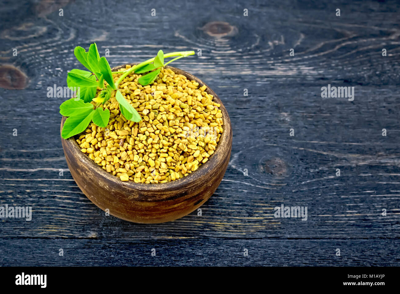 Fenugreek in a clay bowl with a green leaf on a background of a black wooden board Stock Photo