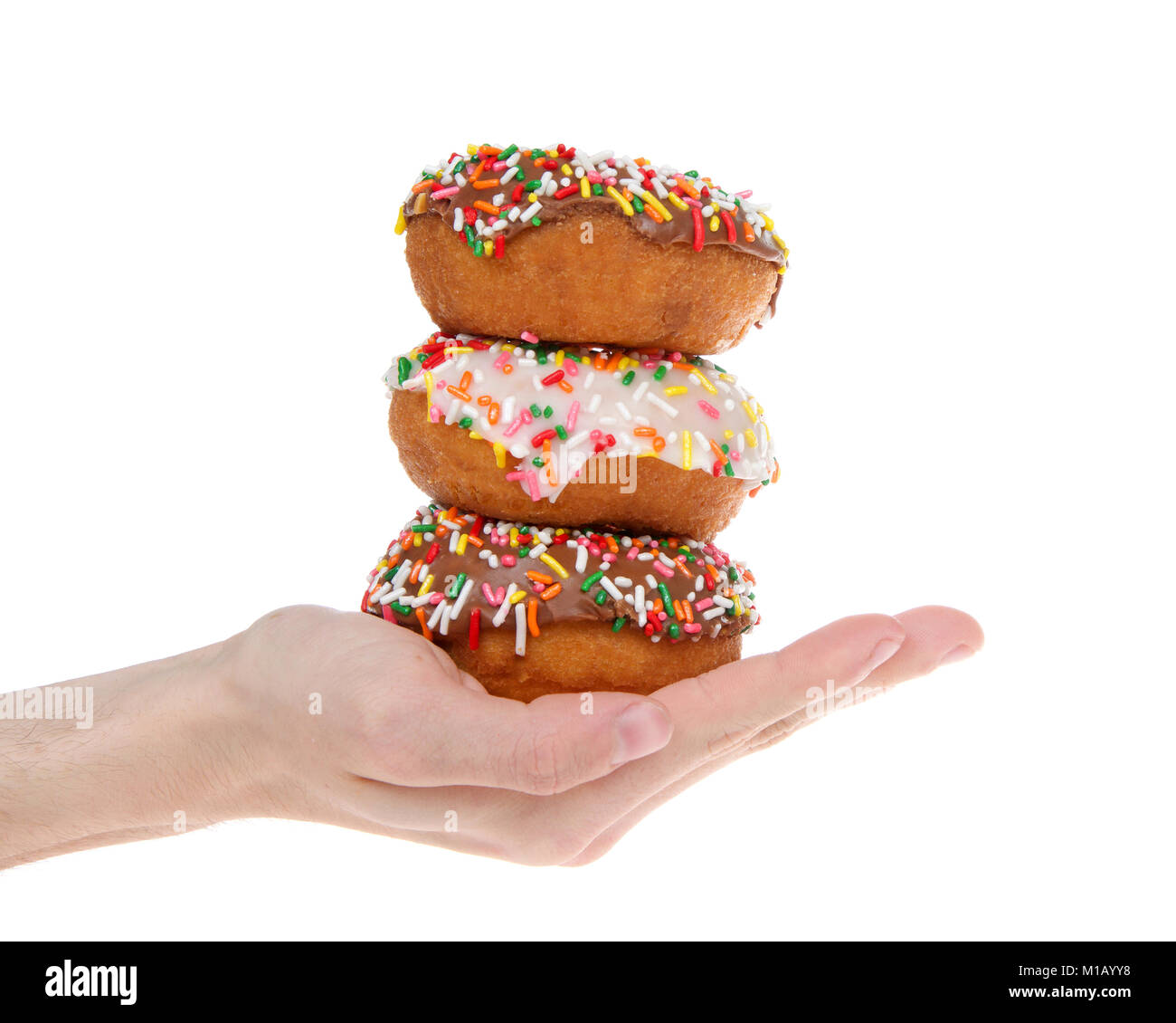 Cake donuts frosted with chocolate and vanilla frosting, rainbow candy sprinkles, stacked and held in the hand of a young male caucasian hand isolated Stock Photo