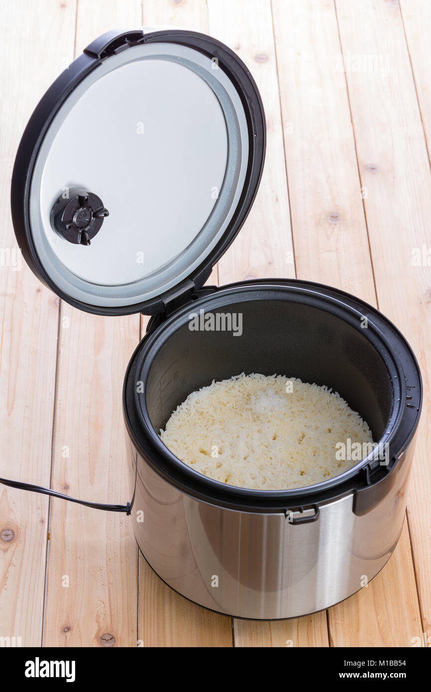 Open electric steamer pot with long grain white rice inside in a high angle view of the contents on a wooden table Stock Photo