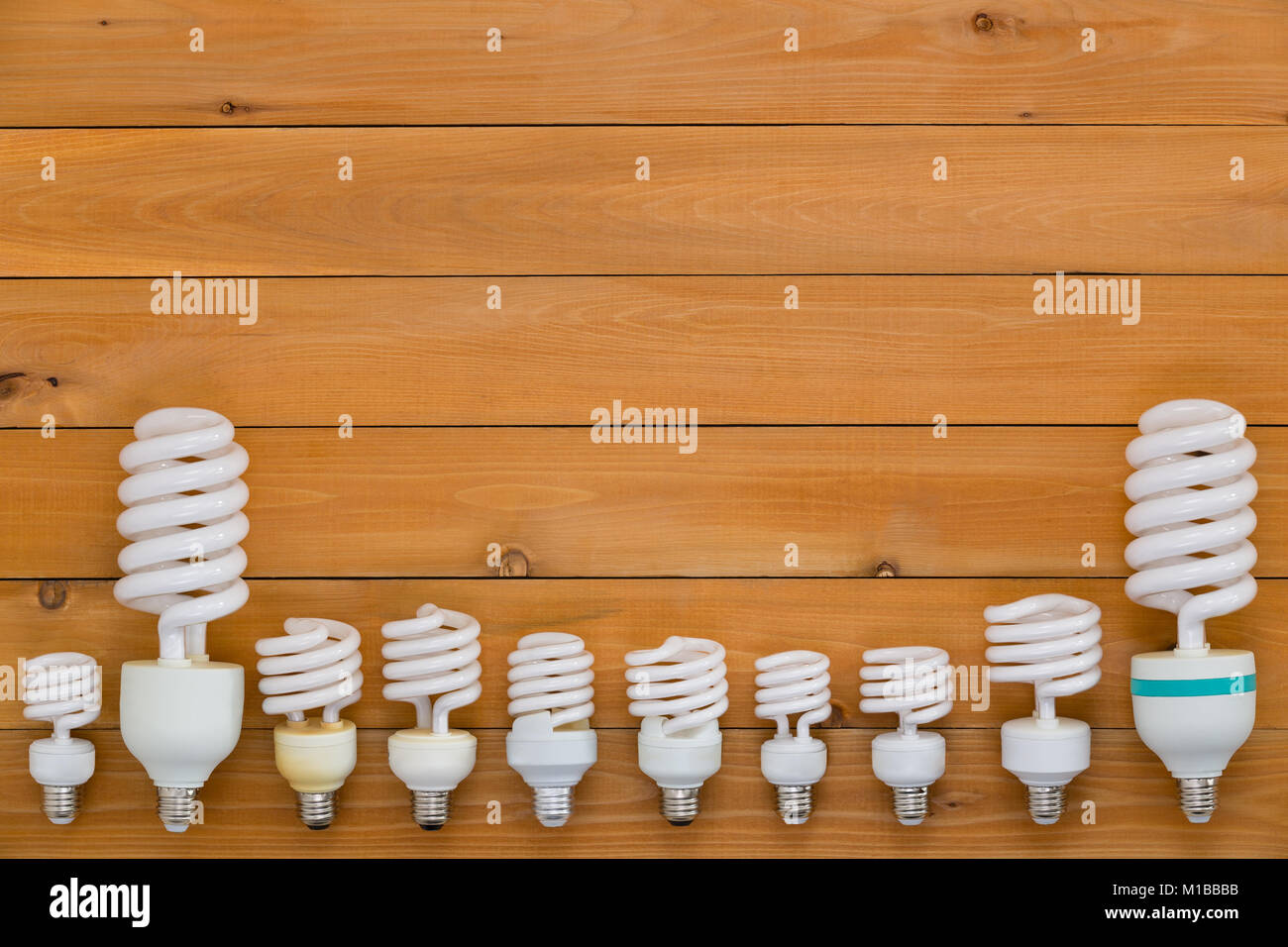 Border of assorted sized energy efficient spiral light bulbs in a row across the bottom of a natural wood background with copy space Stock Photo