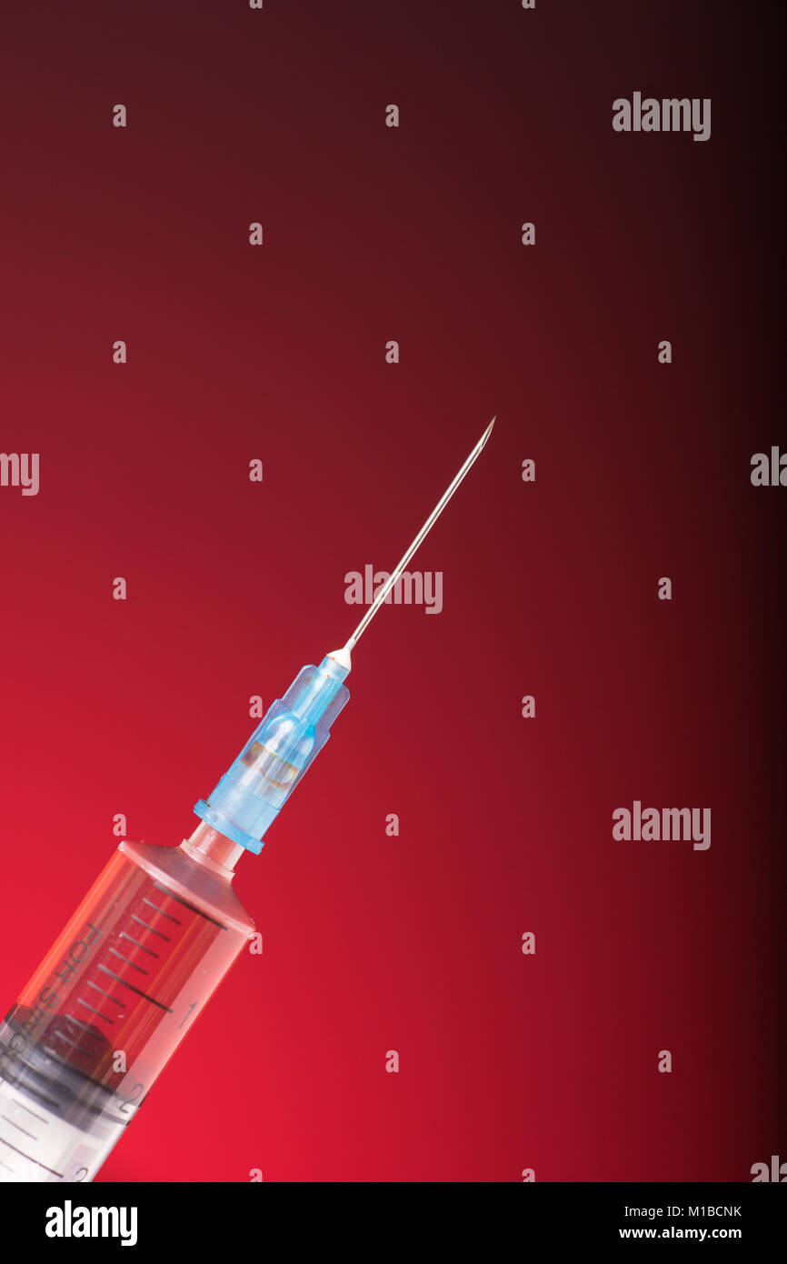Isolated medical syringe on red, dark background Stock Photo