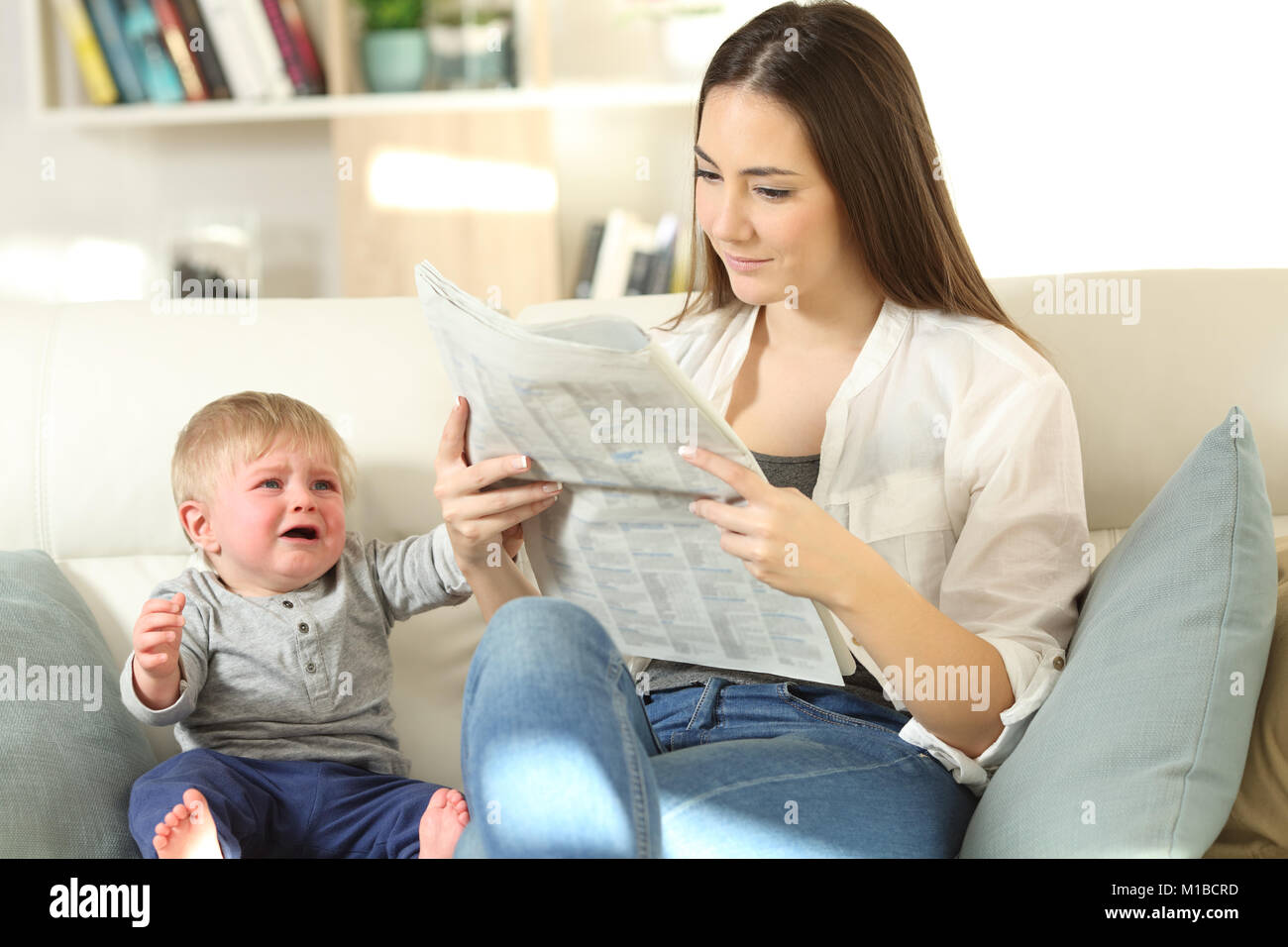 Baby crying demanding attention and his mother ignoring him sitting on a couch in the living room at home Stock Photo