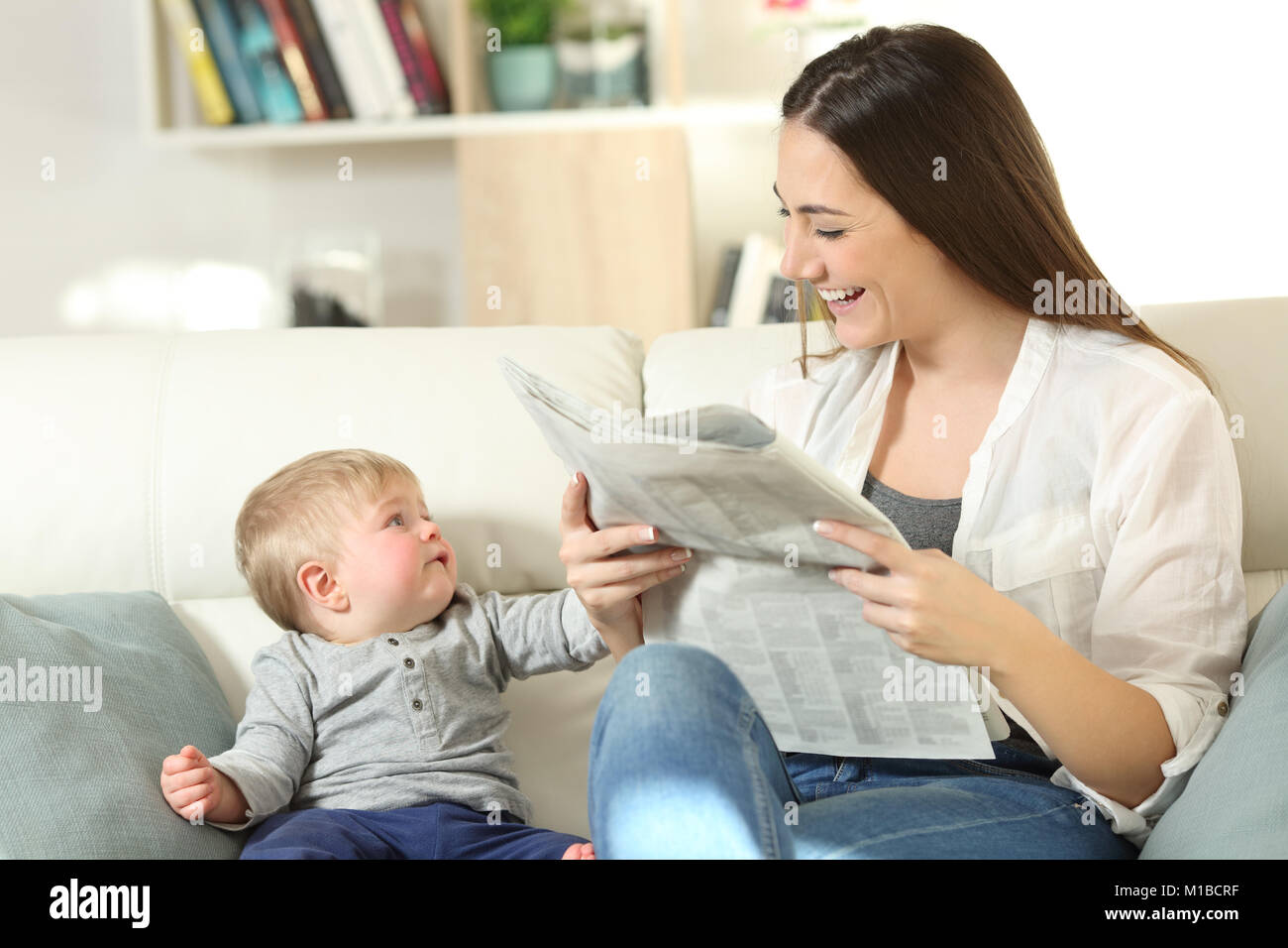 Baby demanding attention of his mother sitting on a couch in the living room at home Stock Photo