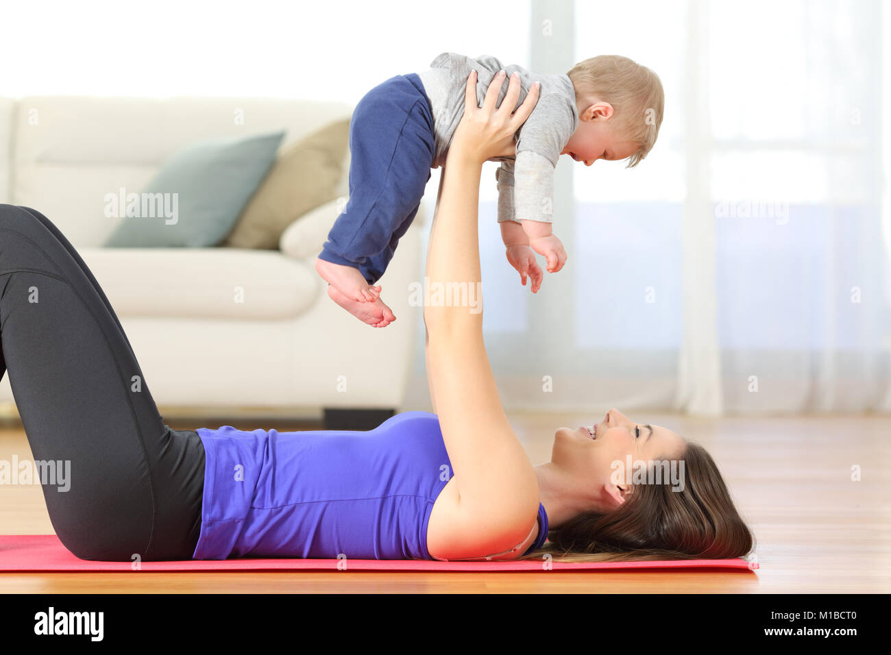 Side view portrait of a happy mother exercising raising her baby on the floor at home Stock Photo