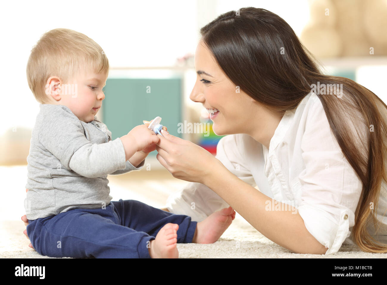 Side view portrait of a proud mother giving a pacifier to her baby on the floor at home Stock Photo