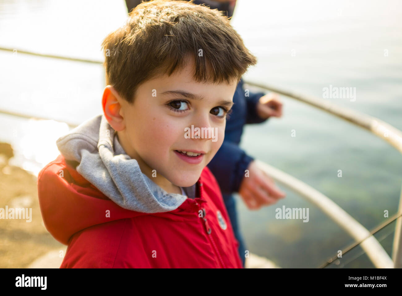 portrait of 9 year old boy with red jacket outside, as a lake
