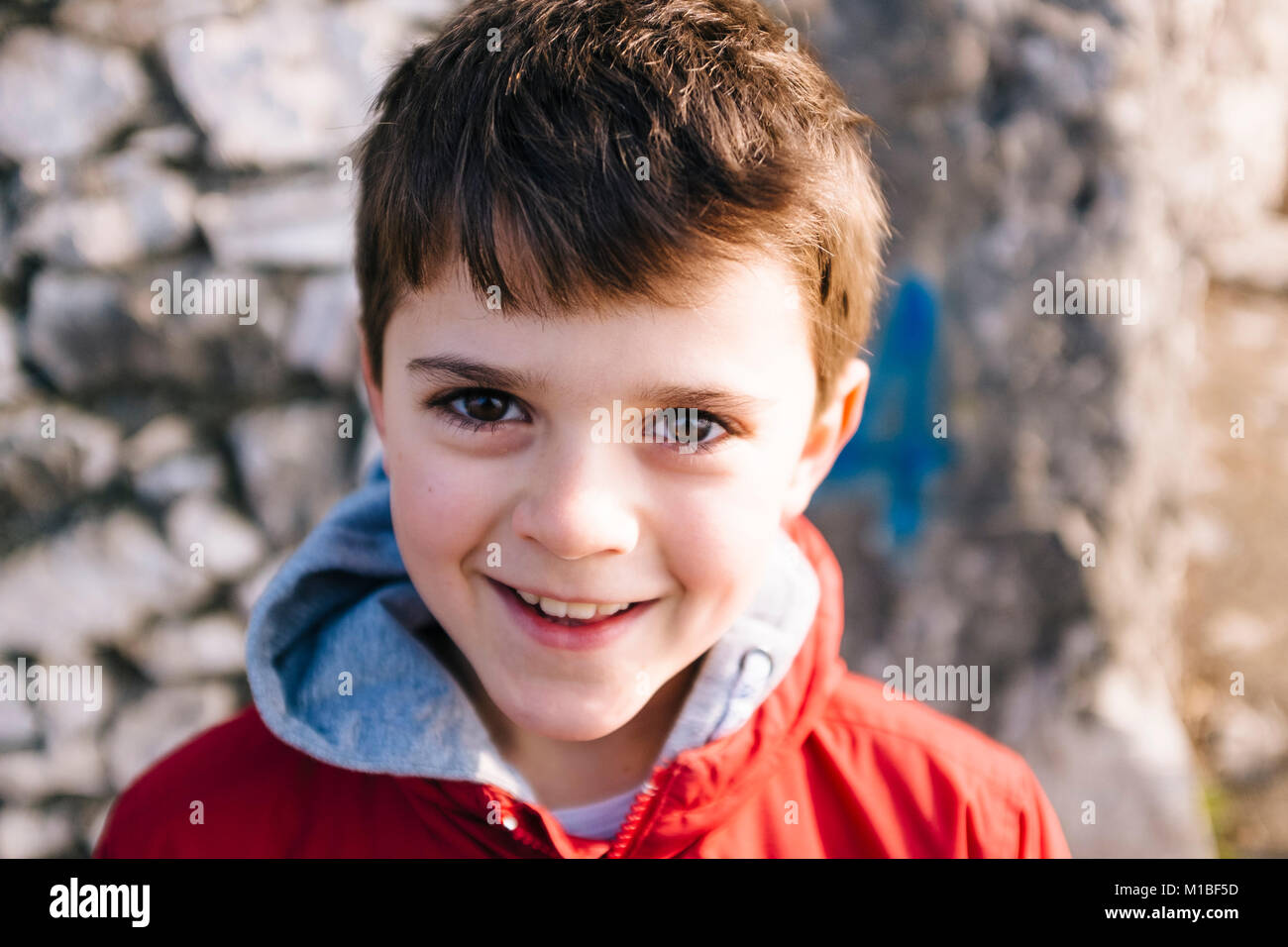portrait of 9 year old boy with red jacket outside, as a big rock
