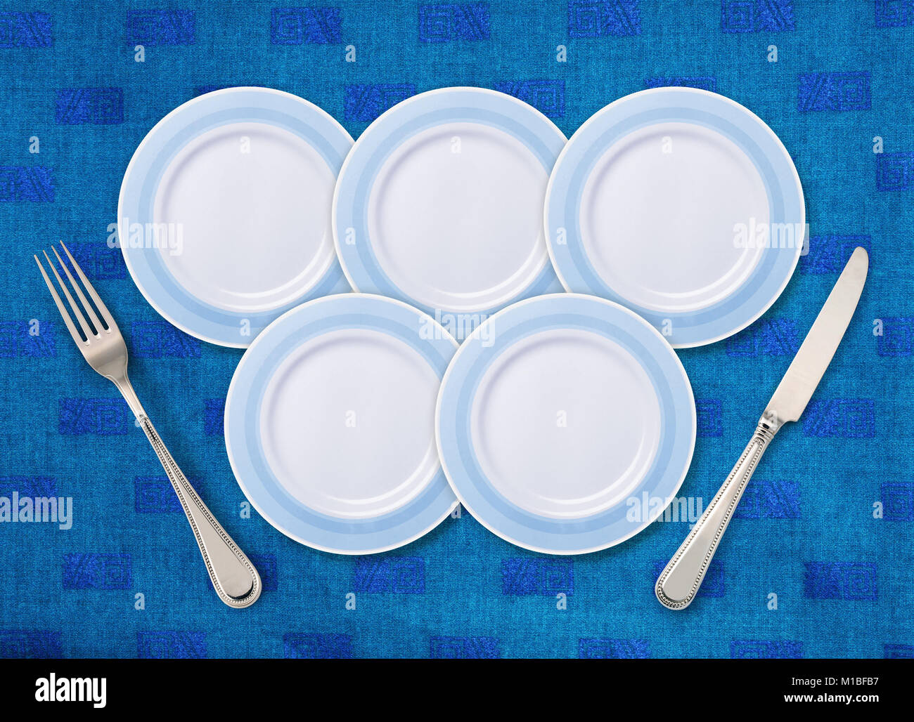 Five white plates on restaurant table that is placed as the Olympic rings, and knife with fork. Stock Photo