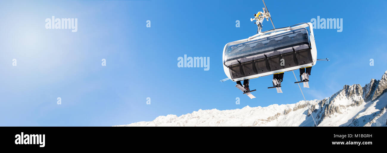 winter vacation - skiers in a chairlift against blue sky at ski resort with copy space Stock Photo