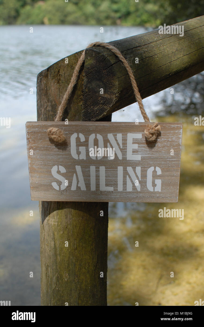 Gone Sailing - a driftwood sign hanging on a wooden fence next to a lake. Stock Photo