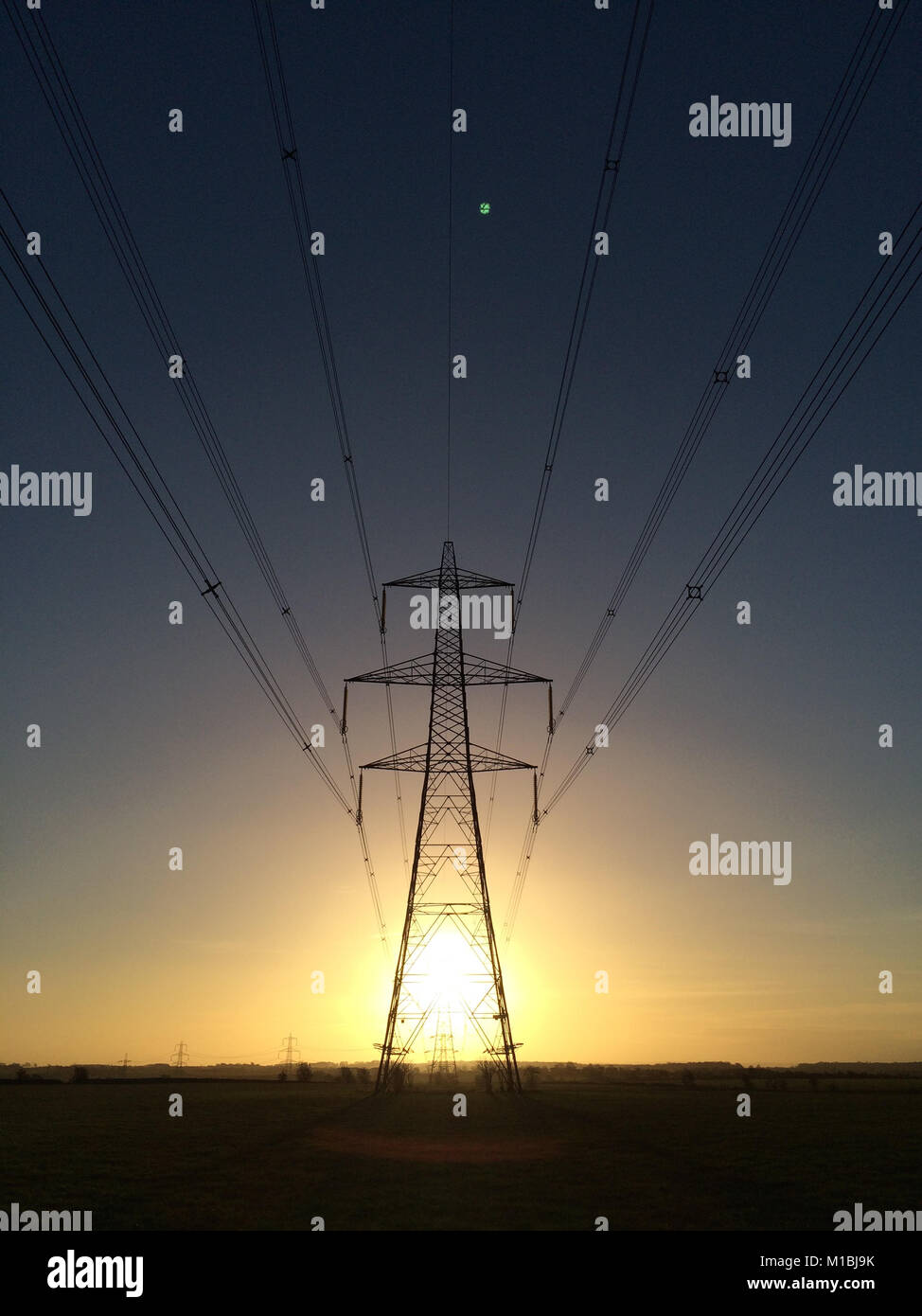 Electricity pylon at sunrise with sun bursting though showing energy and light. Stock Photo