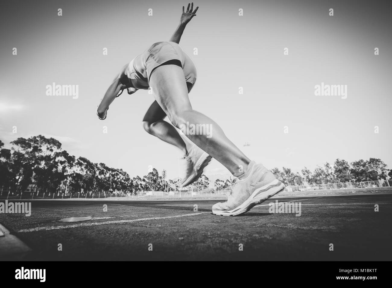 Female fitness model and track athlete sprinting on an athletics track made from tartan Stock Photo