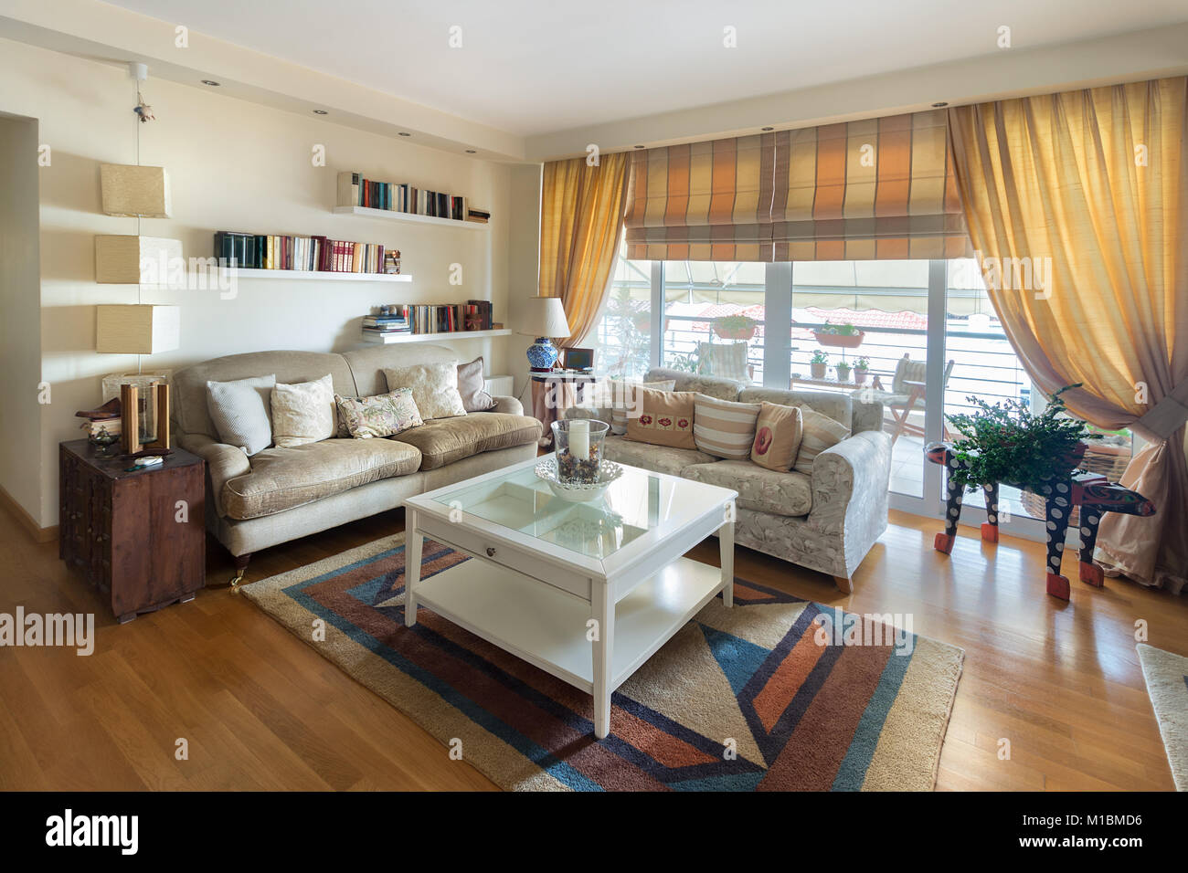 A large living room warm contemporary style with two sofas of two seaters, lamps, coffee table, carpet and stands on the wall with books. The floor is Stock Photo