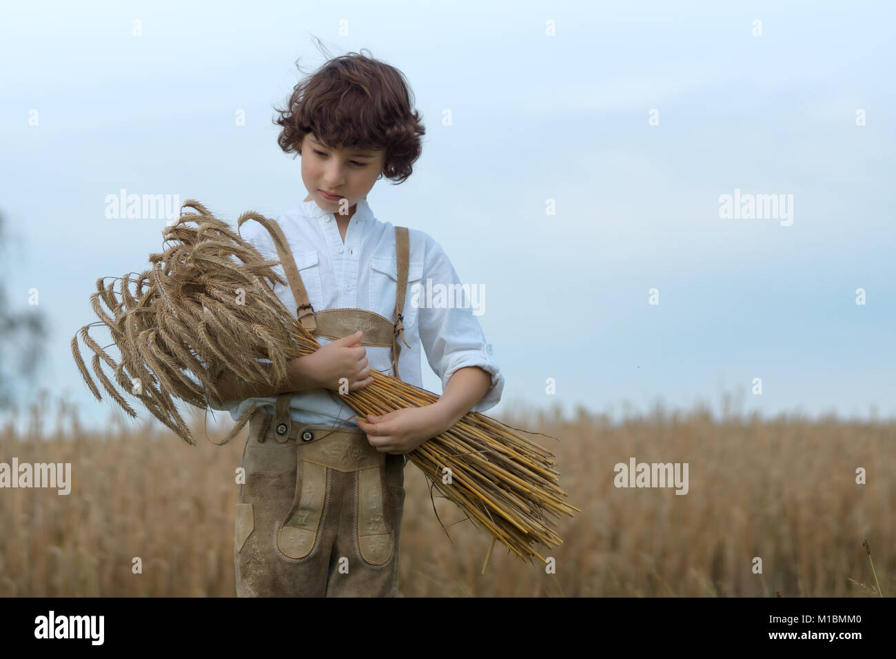 A boy in traditional Bavarian clothes stands in the field and holds a