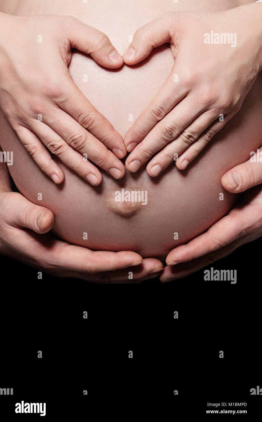 Parents Hands Making a Heart on the Belly of the Pregnant Mother. Parental Love and Care Stock Photo
