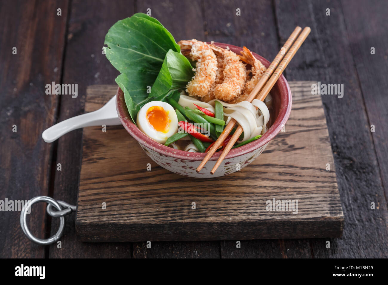 Asian spicy seafood noodle soup with tempura shrimp and greens, close
