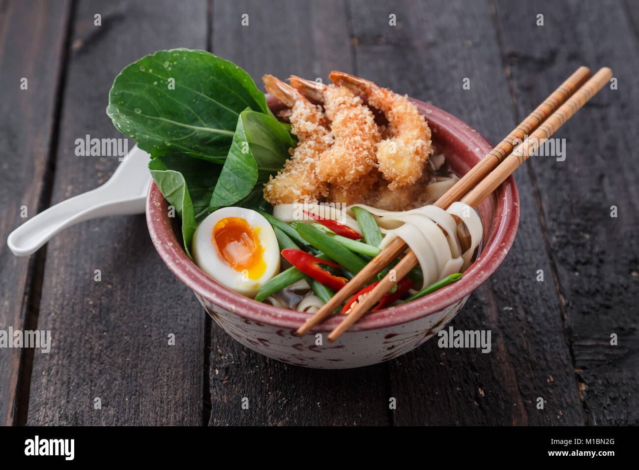 Asian spicy seafood noodle soup with tempura shrimp and greens, close