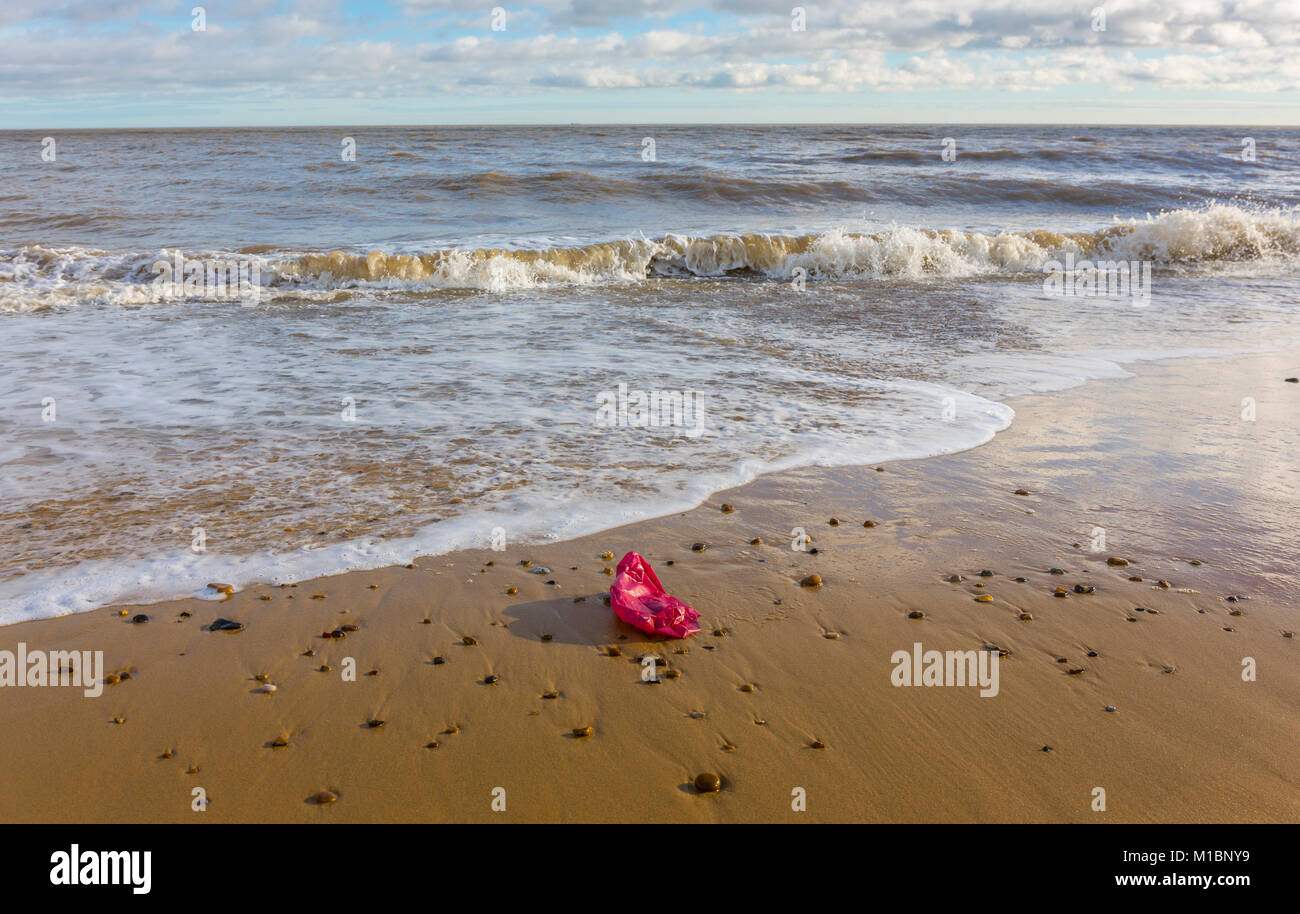 A red plastic bag - litter/pollution on the seashore. The North sea at Southwold, Suffolk. Stock Photo