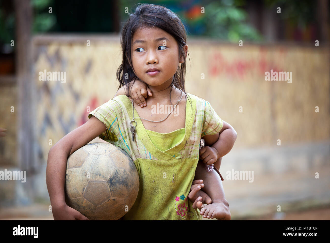 Young girl with football an her littlesister on the back in Lao Village, Northern Laos, Southeast Asia Stock Photo