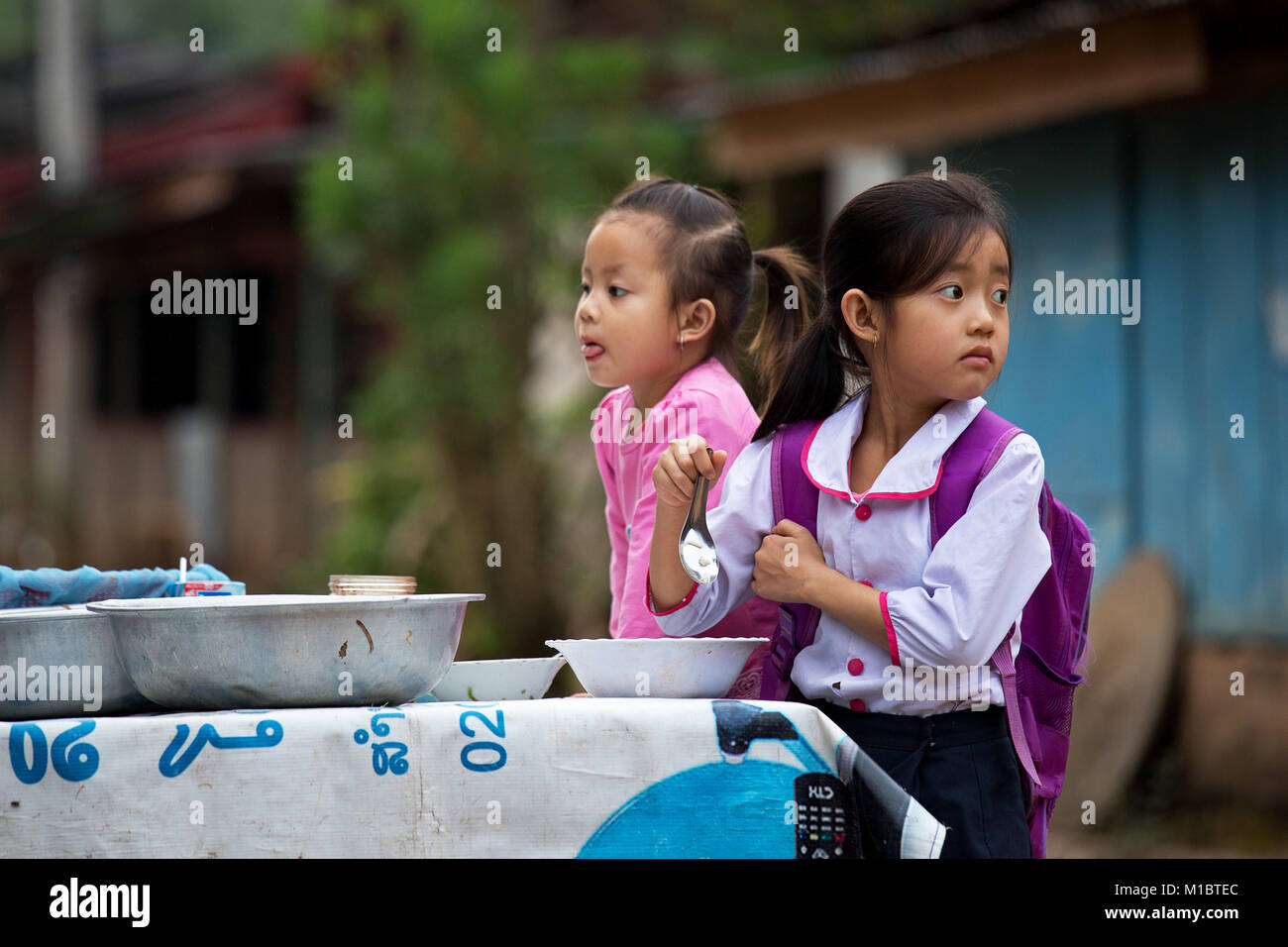 Young laotian girls having breakfast at street before school in Muang Ngoi, Northern Laos, Asia Stock Photo