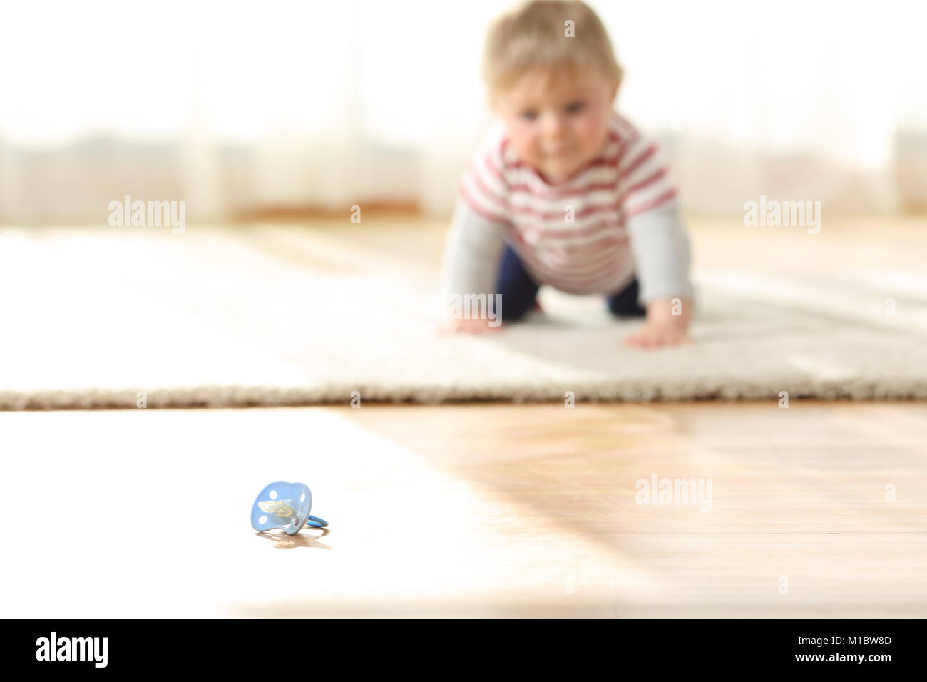 Curious baby crawling towards a dirty pacifier on the floor at home Stock Photo