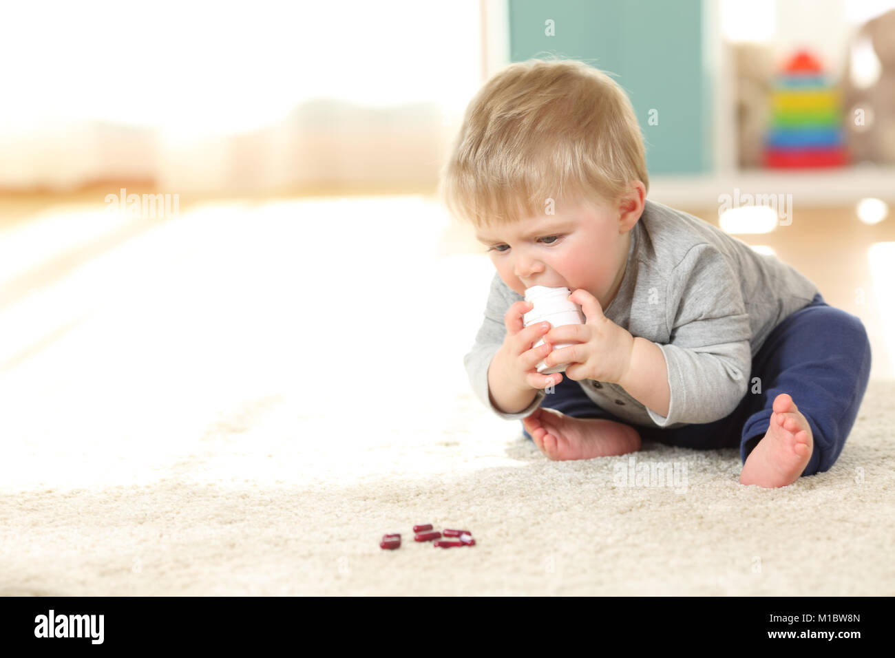 Baby in danger playing with a bottle of medicines on the floor at home Stock Photo