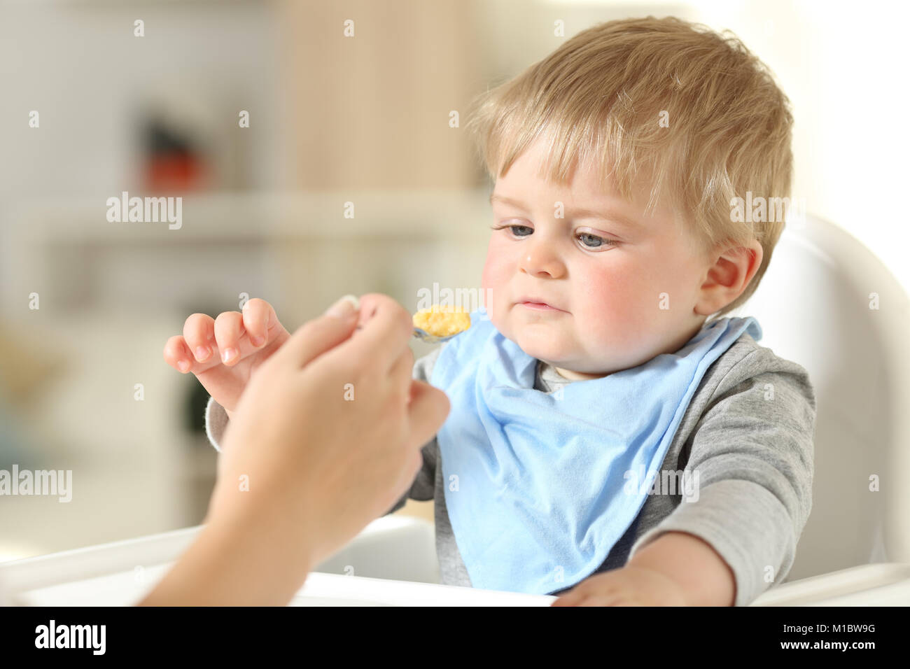 Close up of a mother hand feeding her relaxed baby sitting in a high chair Stock Photo