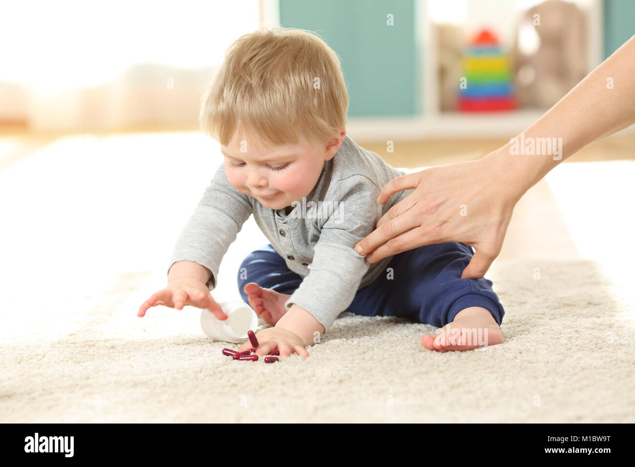 Mother hand preventing the baby from eating pills on the flor at home Stock Photo