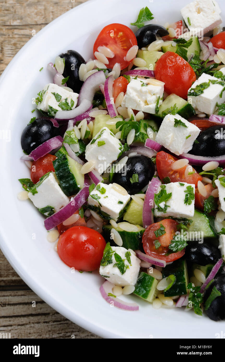 Greek salad orzo pasta with black olive, red onion and cucumber, cherry tomatoes, feta and herbs. Vertically shot. View from above Stock Photo