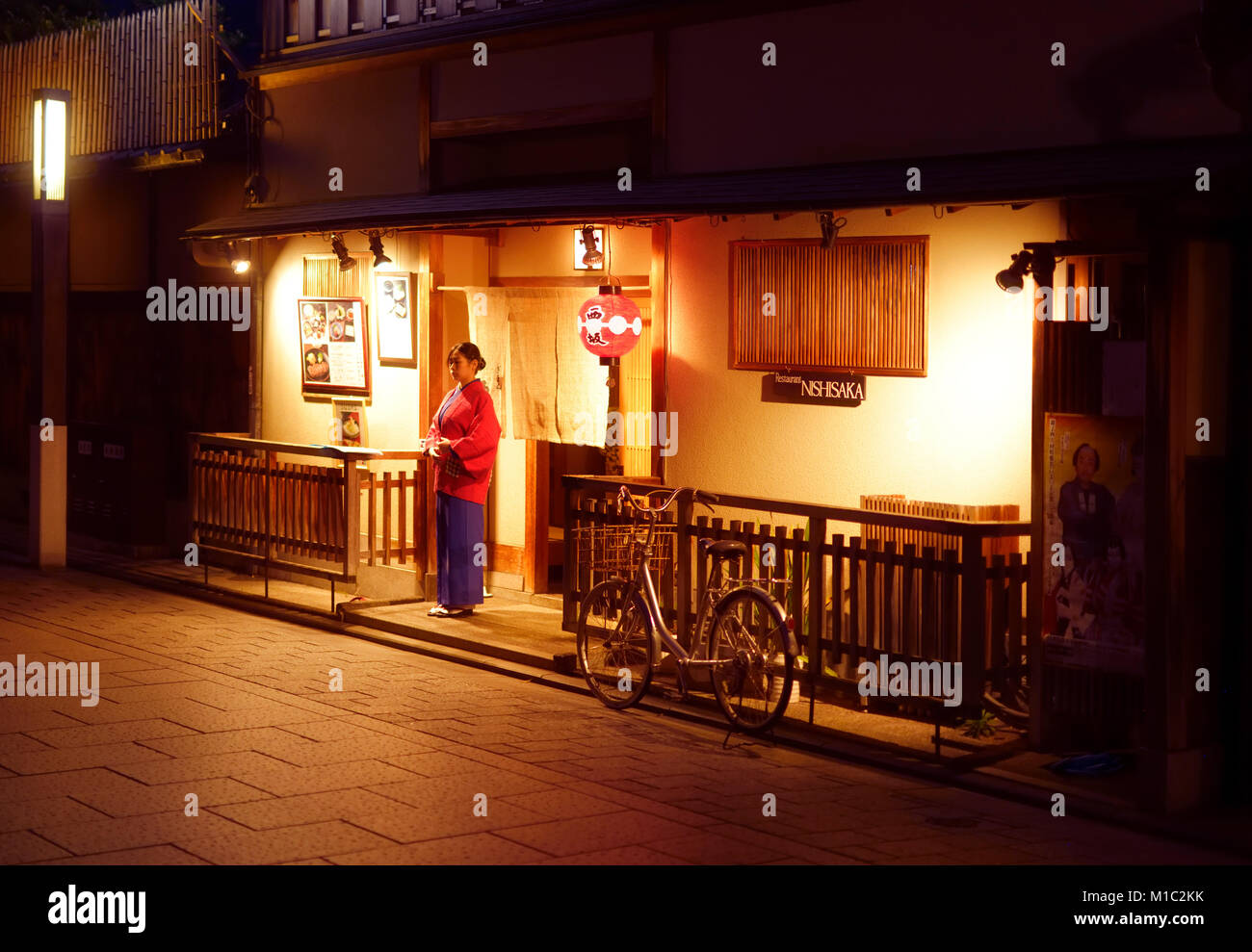 Woman, restaurant clerk welcoming guests by the entrance of a traditional Japanese restaurant Nishisaka at night on Hanamikoji Dori street in Gion dis Stock Photo