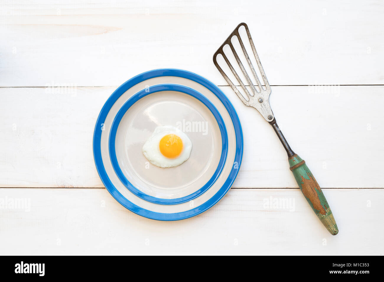 Fried Quail Egg on a cornishware plate with a vintage spatula from above Stock Photo